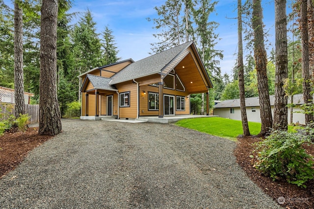 exterior space with a lawn, gravel driveway, a shingled roof, and fence
