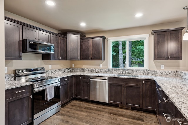 kitchen with dark wood finished floors, light stone counters, stainless steel appliances, a sink, and dark brown cabinetry