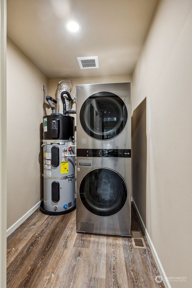 laundry area featuring visible vents, wood finished floors, water heater, stacked washer / drying machine, and laundry area