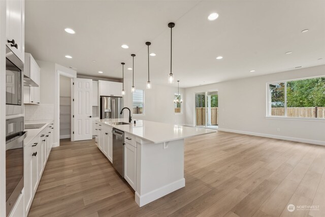 kitchen featuring stainless steel appliances, a large island with sink, light countertops, white cabinetry, and a sink