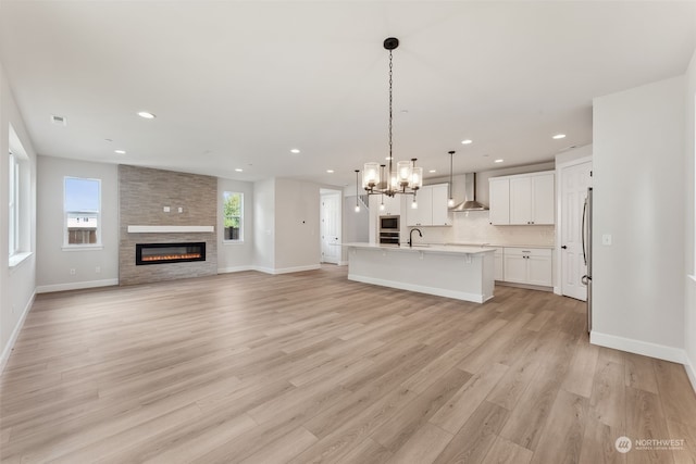 unfurnished living room with a notable chandelier, sink, a fireplace, and light hardwood / wood-style floors