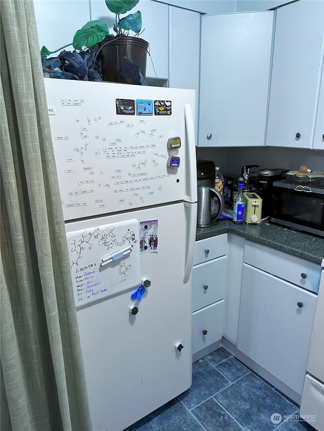 kitchen with white cabinetry, dark tile patterned floors, and white fridge