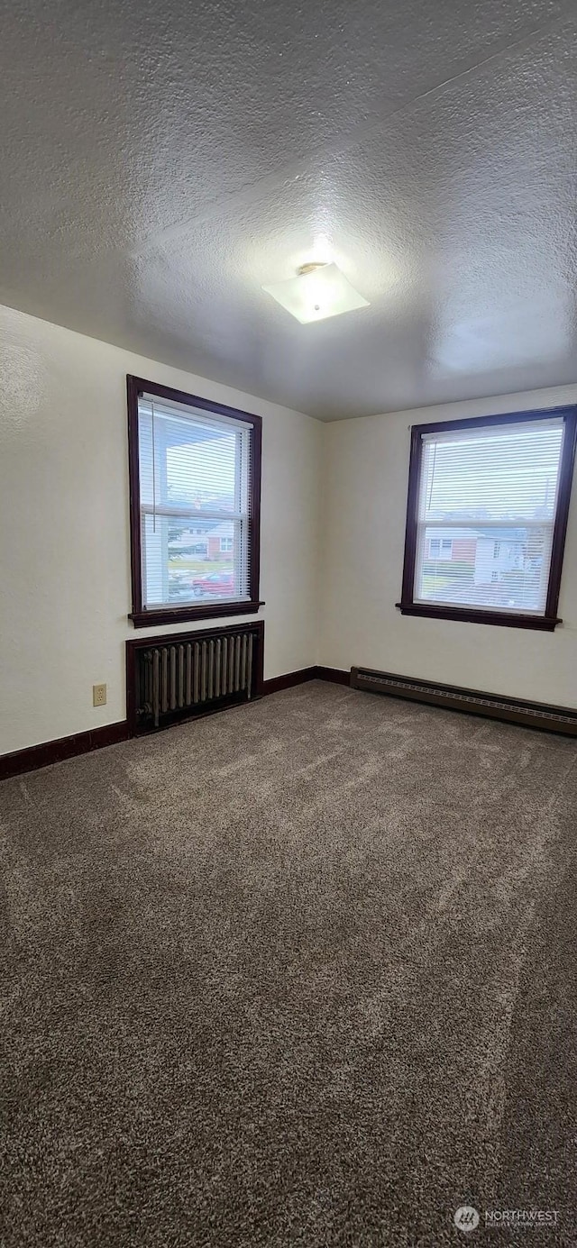 carpeted spare room featuring radiator heating unit, plenty of natural light, a textured ceiling, and a baseboard heating unit