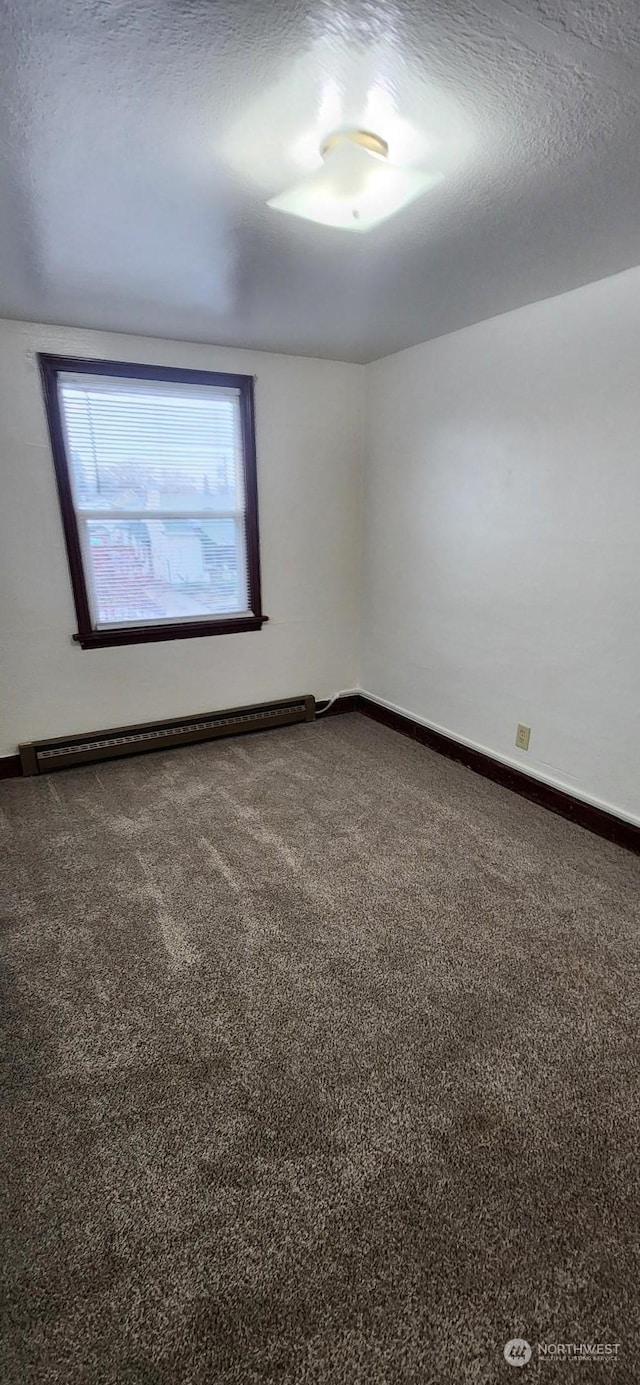 carpeted empty room featuring a baseboard heating unit and a textured ceiling