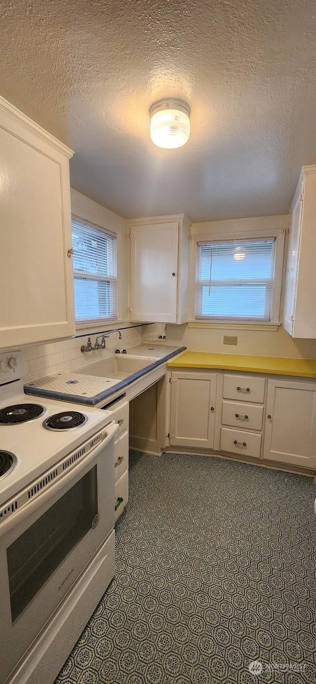 kitchen featuring a textured ceiling, white electric range oven, sink, and white cabinetry