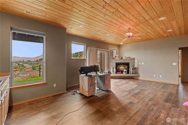 office with wood ceiling, ceiling fan, wood-type flooring, a tiled fireplace, and a mountain view