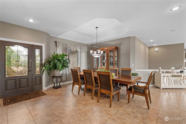 dining space with light tile patterned flooring, an inviting chandelier, and a tray ceiling