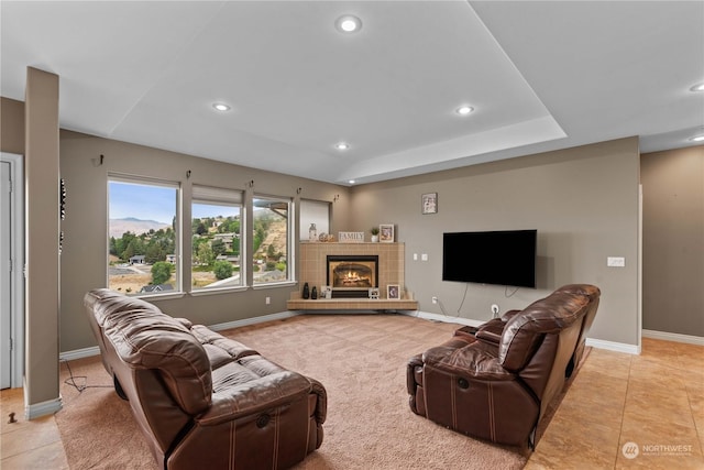 living room with a tray ceiling, a tile fireplace, and light tile patterned floors