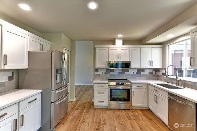 kitchen featuring appliances with stainless steel finishes, light hardwood / wood-style flooring, sink, backsplash, and white cabinetry