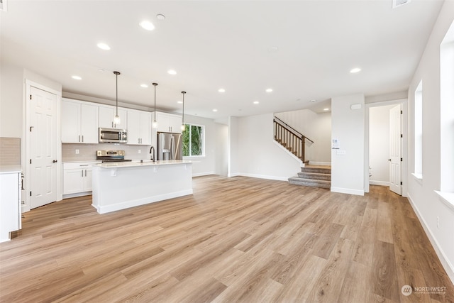 kitchen featuring sink, white cabinets, hanging light fixtures, stainless steel appliances, and a center island with sink