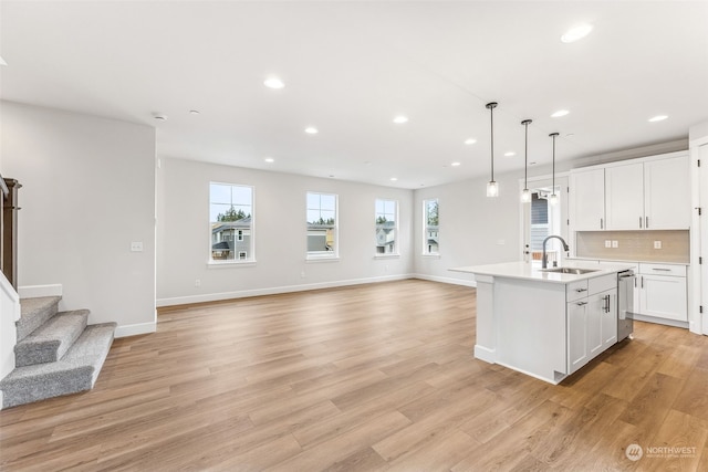 kitchen with sink, light hardwood / wood-style flooring, hanging light fixtures, white cabinets, and a center island with sink