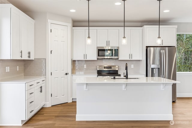 kitchen with white cabinetry, appliances with stainless steel finishes, decorative light fixtures, and an island with sink