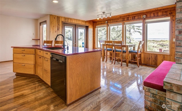 kitchen with wood walls, a sink, black dishwasher, and dark wood finished floors