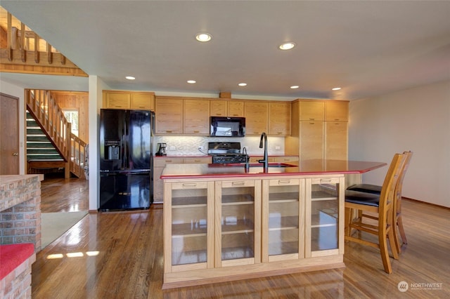 kitchen with wood finished floors, a sink, black appliances, an island with sink, and recessed lighting