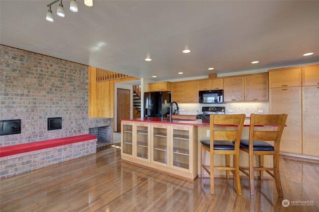 kitchen with black appliances, backsplash, light wood-style floors, and a fireplace