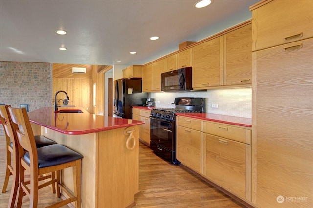 kitchen featuring a sink, black appliances, light wood-style floors, a breakfast bar area, and recessed lighting
