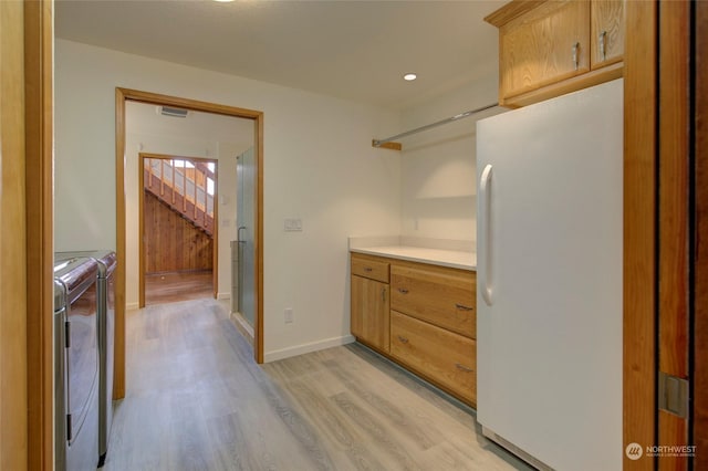 kitchen with light wood-type flooring, freestanding refrigerator, light countertops, baseboards, and independent washer and dryer