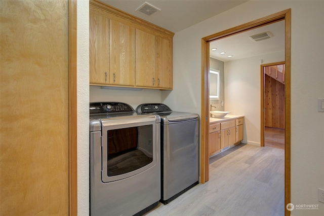 washroom with light wood finished floors, visible vents, a sink, independent washer and dryer, and cabinet space