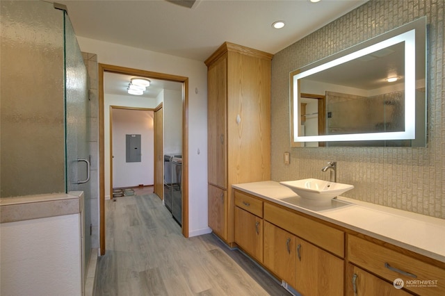 full bath featuring wood finished floors, a stall shower, separate washer and dryer, vanity, and electric panel