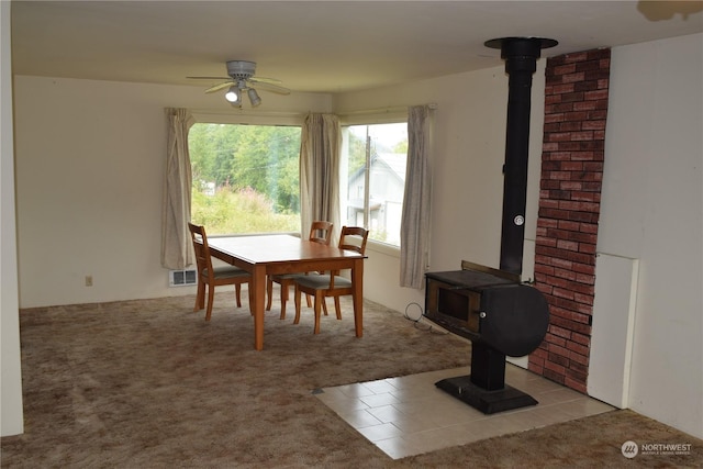 dining space with carpet, a wood stove, visible vents, and ceiling fan