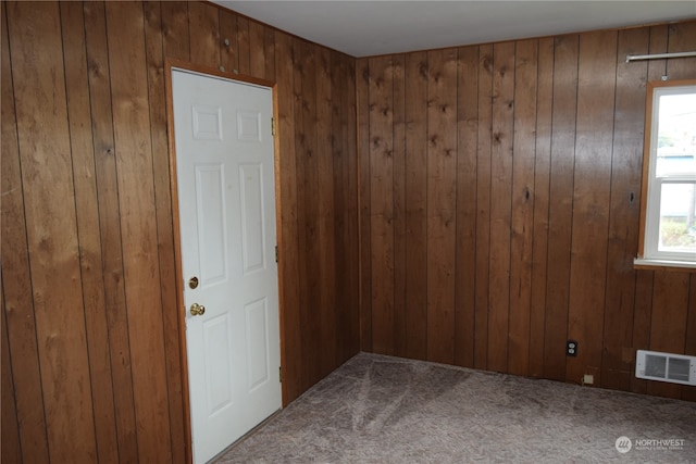 carpeted empty room featuring wood walls and visible vents