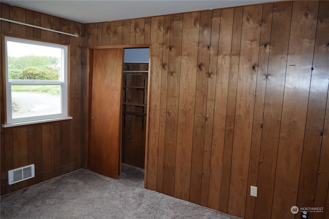 unfurnished bedroom with carpet, visible vents, and wooden walls