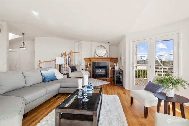 living room with a tiled fireplace, vaulted ceiling, and light hardwood / wood-style floors