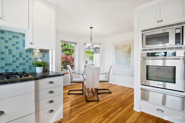 kitchen with decorative backsplash, stainless steel appliances, white cabinets, and light wood-type flooring