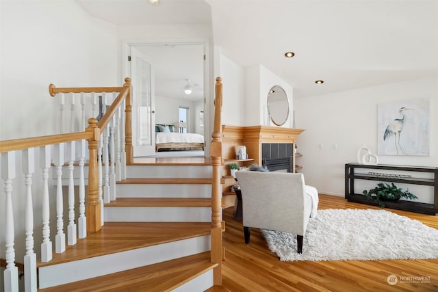 staircase with hardwood / wood-style flooring, ceiling fan, and a fireplace