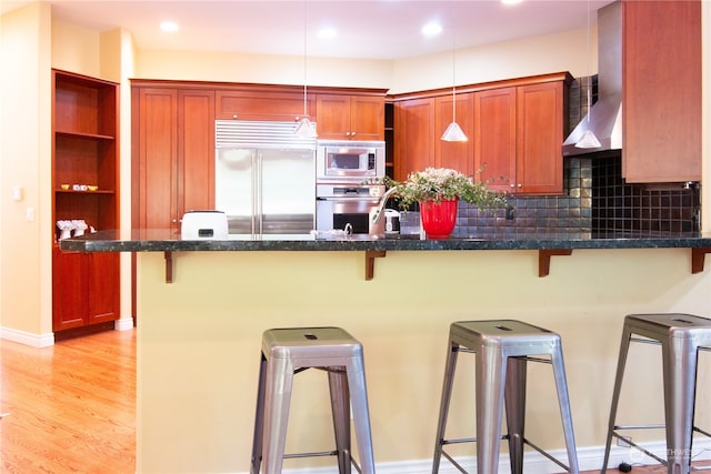 kitchen with backsplash, built in appliances, decorative light fixtures, light hardwood / wood-style floors, and a breakfast bar area