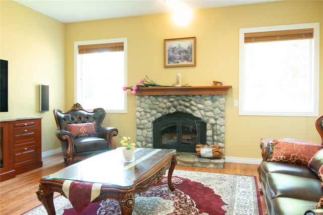 living room featuring a stone fireplace, plenty of natural light, and light wood-type flooring