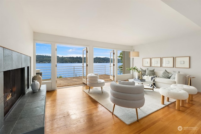 living area with a water view, a tiled fireplace, and wood finished floors