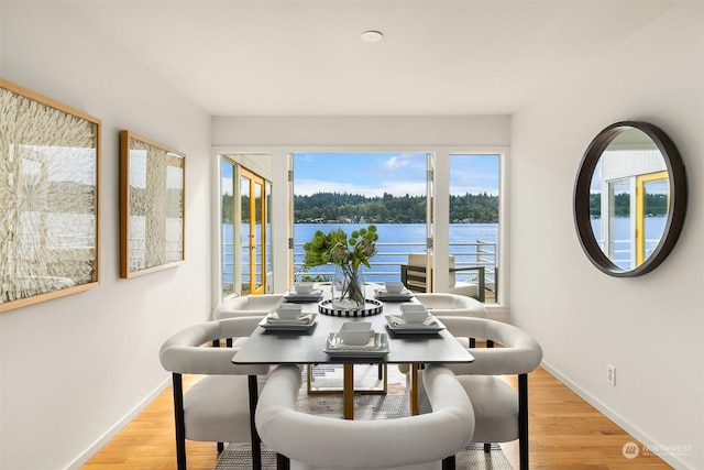 dining space with light wood finished floors, a water view, and baseboards