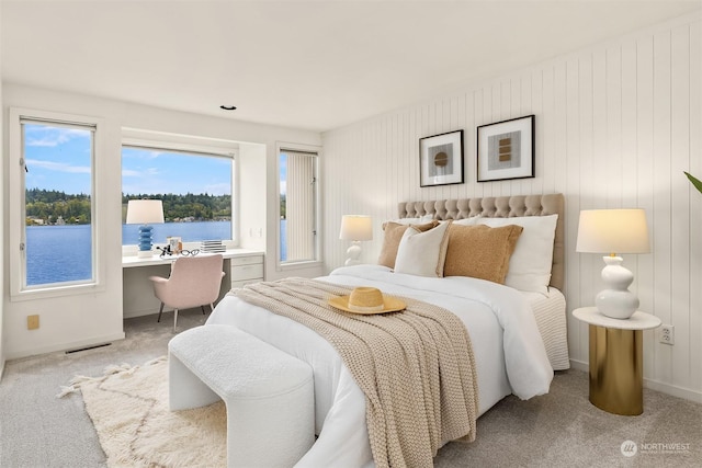 bedroom featuring a water view, visible vents, built in desk, and light colored carpet