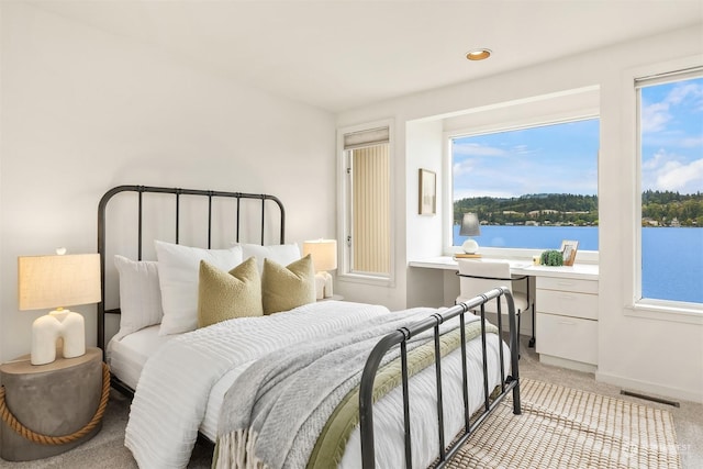 bedroom with light colored carpet, a water view, visible vents, baseboards, and built in study area