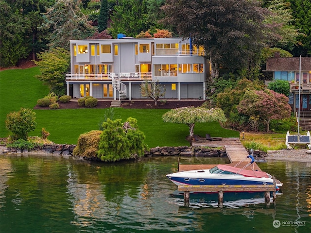 back of house with a balcony, boat lift, a water view, stairs, and a yard