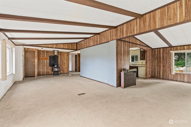 unfurnished living room with wood walls, light colored carpet, and vaulted ceiling with beams