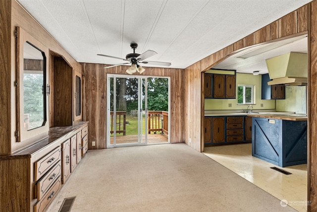 interior space featuring ceiling fan, premium range hood, wooden walls, and plenty of natural light