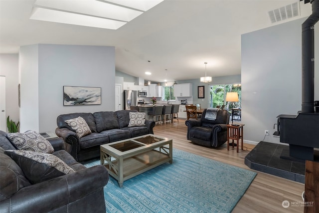 living room with a wood stove, light hardwood / wood-style flooring, a notable chandelier, and vaulted ceiling