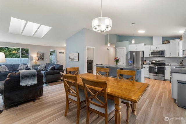 dining space featuring lofted ceiling with skylight, sink, and light hardwood / wood-style floors