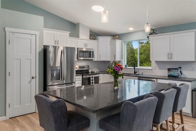 kitchen with white cabinetry, a kitchen island, stainless steel appliances, a kitchen bar, and vaulted ceiling