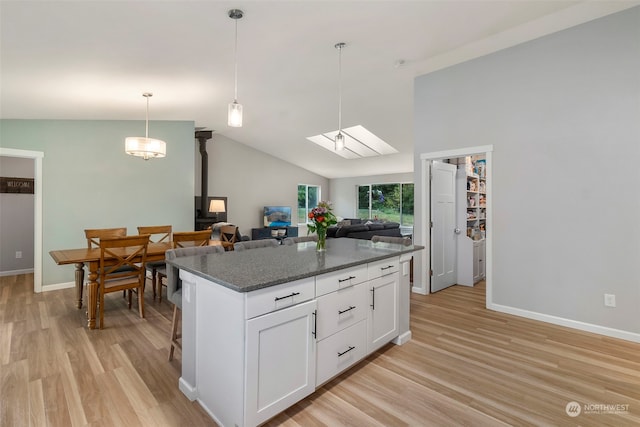 kitchen with dark stone countertops, white cabinets, hanging light fixtures, a center island, and light hardwood / wood-style flooring