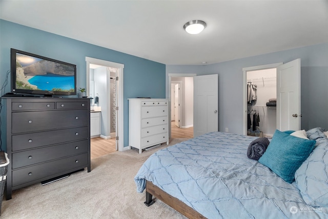 bedroom with light colored carpet, ensuite bath, a closet, and a walk in closet