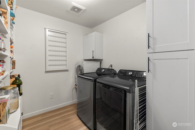 clothes washing area featuring separate washer and dryer, light hardwood / wood-style flooring, and cabinets