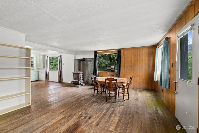 dining room featuring a wood stove, a textured ceiling, wooden walls, and dark wood-type flooring