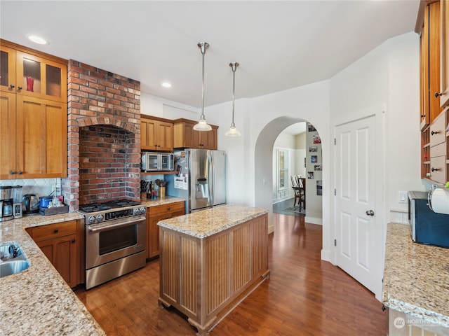 kitchen with a kitchen island, dark hardwood / wood-style floors, pendant lighting, appliances with stainless steel finishes, and light stone counters