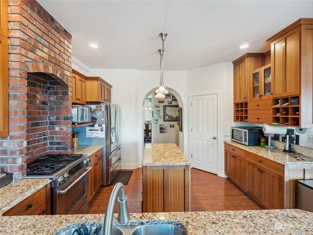 kitchen with pendant lighting, light stone countertops, stainless steel appliances, and wood-type flooring