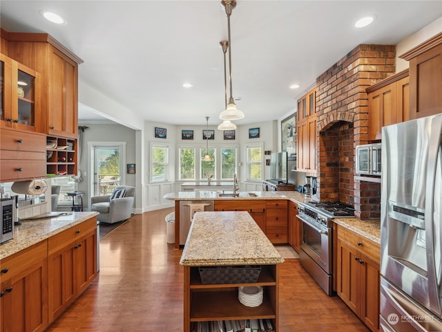 kitchen featuring light stone countertops, a center island, hanging light fixtures, hardwood / wood-style floors, and stainless steel appliances