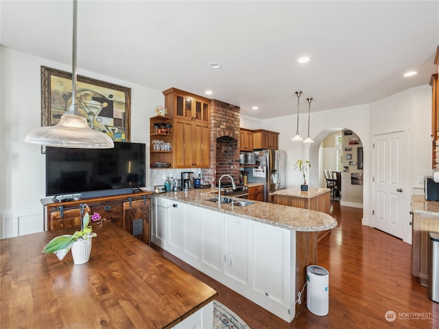 kitchen featuring light stone counters, a kitchen island with sink, decorative light fixtures, and stainless steel appliances