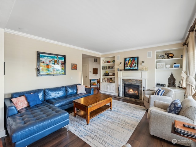 living room with crown molding, a stone fireplace, built in features, and dark hardwood / wood-style flooring